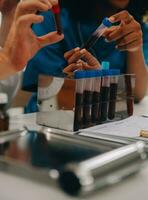 Medical worker in lab coat and sterile mask, doing a microscope analysis while her colleague are working behind photo