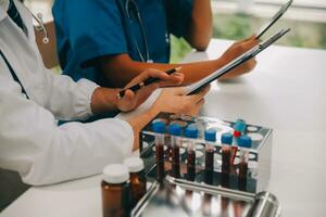 Medical worker in lab coat and sterile mask, doing a microscope analysis while her colleague are working behind photo