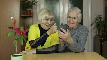 Pretty mature senior couple grandparents enjoy online shopping on phone at home video