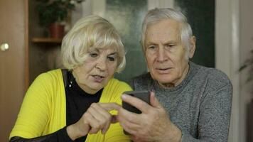 Pretty mature senior couple grandparents enjoy online shopping on phone at home video