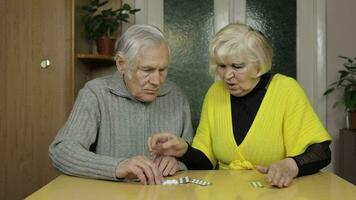 Old senior grandparents looking at pills, tablets in a blisters on table at home video