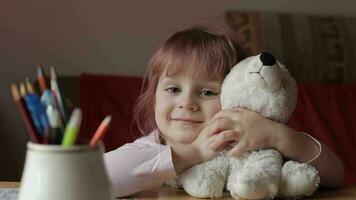 fofa pequeno criança menina sentado às casa jogando e abraçando dela Urso de pelúcia Urso brinquedo video