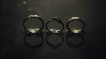 Wedding and engagement rings lying on dark water surface shining with light video