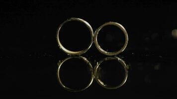 Wedding rings on dark water surface shining with light. Close up macro video