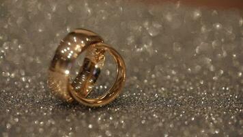 Wedding gols rings lying on shiny glossy surface. Shining with light. Close-up video