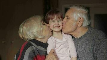 Grandfather and grandmother kissing on cheeks their kid granddaughter at home video