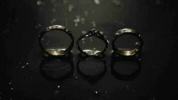 Wedding and engagement rings lying on dark water surface shining with light video