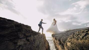 Groom goes to bride and gives her a hand. Newlyweds on mountainside by the sea video