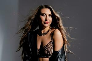 Model with luxurious hair flowing from a gust of wind in a black raincoat and seductive lingerie photo