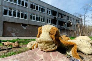 dirty toys on the background of a burned-out destroyed school in an abandoned city in Ukraine photo