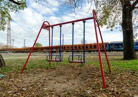 empty swings on an empty playground without people against the background of burnt trains in Ukraine photo