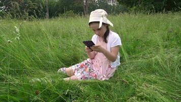 menina senta dentro uma campo e parece às uma Smartphone video