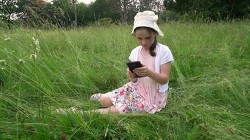 Mädchen sitzt im ein Feld und sieht aus beim ein Smartphone video
