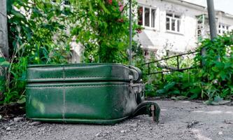 old suitcase against the background of a destroyed house in an abandoned city in Ukraine photo