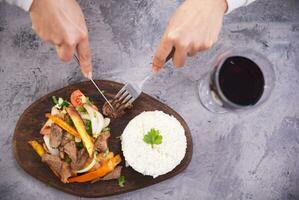 Hands picking up a piece of meat with a fork and knife, from a typical Peruvian dish called Lomo saltado, seen from above. photo