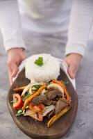 Hands taking a dish named Lomo saltado served on a wooden board. photo