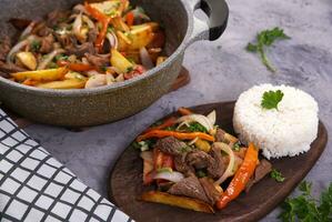 Hands picking up a piece of meat with a fork and knife, from a typical Peruvian dish called Lomo saltado, seen from above. photo