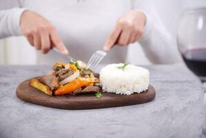 Hands picking up a piece of meat with a fork and knife, from a typical Peruvian dish called Lomo saltado. photo