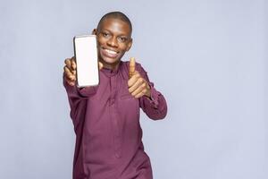 Portrait Young smiling happy balck african man 20s in hold in hand use mobile cell phone with blank screen workspace area show thump up gesture isolated on plain white background studio photo