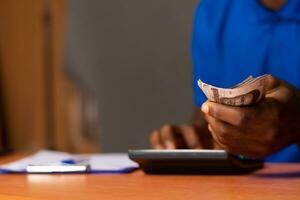 nigerian man holding money, and using a calculator photo