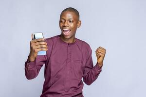 happy black guy in authentic african costume using mobile phone, white background, copy space photo