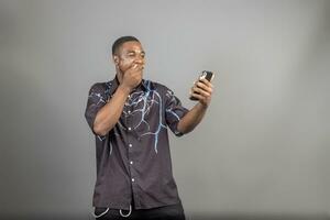 Cheerful millennial black man in casual using modern smart phone, checking social media, looking at copy space for mobile application photo