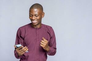 Portrait of a cheerful young man wearing african clothes standing isolated over white studio background, using mobile phone photo