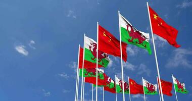 Galles e Cina bandiere agitando insieme nel il cielo, senza soluzione di continuità ciclo continuo nel vento, spazio su sinistra lato per design o informazione, 3d interpretazione video