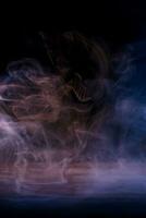 imagen conceptual de humo multicolor aislado sobre fondo negro oscuro y mesa de madera. foto