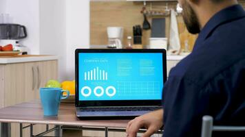 Revealing shot of businessman in the kitchen looking at computer screen with company data and analysis. Working at home. Dolly slider 4K footage video