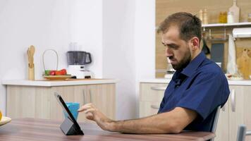 Man surf the web on a digital tablet PC in his kitchen at the table video