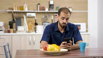 homme à le table dans le cuisine en utilisant une téléphone intelligent. il sourcils le l'Internet. chariot glissière 4k métrage video