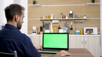 Mann beim das Tabelle im das Küche suchen beim Laptop mit isoliert Grün Bildschirm Chroma Attrappe, Lehrmodell, Simulation video