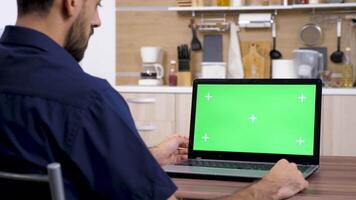 Man in the kitchen looking at computer with green screen mock-up. The chroma has marks for easy keying. Dolly slider 4K footage with parallax effect video