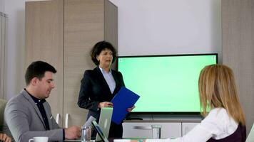 volwassen zakenvrouw in voorkant van groot groen scherm TV met een klembord in handen in de vergadering kamer. dolly schuif 4k beeldmateriaal video