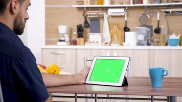 homme à le cuisine à la recherche à numérique tablette PC avec vert écran chrominance moquer en haut video