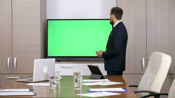 Businessman in conference room pointing to a green screen mock-up TV. Dolly slider 4K footage video