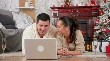 Pareja compras en línea para Navidad regalos. ellos utilizar un ordenador portátil y sentar en el piso en un hermosa decorado habitación video