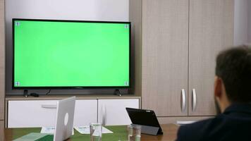 homem de negocios sentado dentro cadeira falando para verde tela televisão dentro encontro sala. boneca controle deslizante 4k cenas video