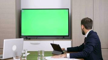 Geschäftsmann im Konferenz Video Anruf über ein groß Grün Bildschirm Fernseher. Dolly Schieberegler 4k Aufnahmen