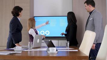 Business partners in the conference room in front of big screen TV with animated data and charts. They talk and analyze the company data video