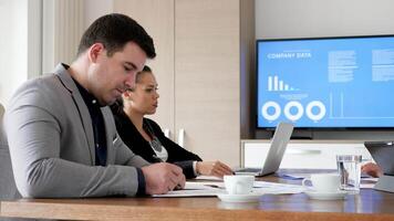 Businessman reading then signing a contract in the conference room while his partners are talking in the background video