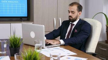 Businessman in meeting room typing on the computer theb he looks at the TV. Dolly slider 4K footage video