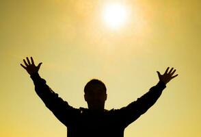 Silhouette of a man against the background of the sun and yellow at sunset sky. Hands are raised up to the sun photo