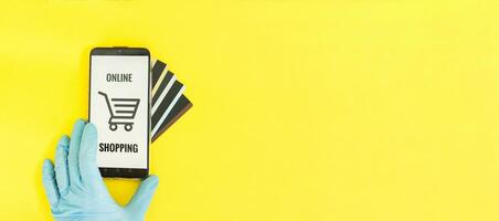 Close-up of hands in medical gloves with a smartphone. Online shopping, online banking, online payment. Payment with plastic cards. Flat Lay on a yellow background. photo