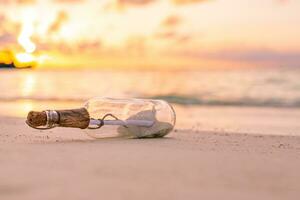 Message in the bottle washed ashore against the sun setting down. Tropical beach sea shore castaway design background photo