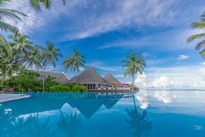 maravilloso paisaje, nadando piscina azul cielo con nubes tropical recurso hotel en Maldivas. fantástico relajarse y pacífico vibras, sillas, tumbonas debajo paraguas y palma hojas. lujo viaje vacaciones foto