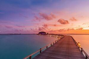 Sunset on Maldives island, luxury water villas resort and wooden pier. Beautiful sky and clouds and beach background for summer vacation holiday and travel concept photo