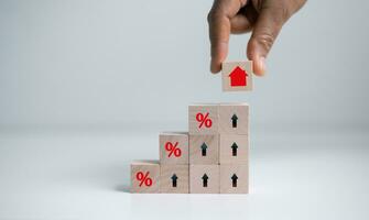 Hand holding house icon with percent sign from stack of blocks with percentage icon. House and property investment and asset management concept. Interest rates, loan mortgage, house tax. photo