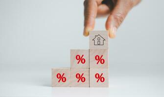 Hand holding house icon with percent sign from stack of blocks with percentage icon. House and property investment and asset management concept. Interest rates, loan mortgage, house tax. photo